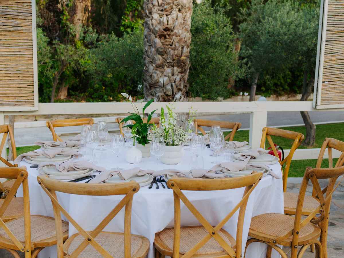 Elegant table setting at a wedding reception with a white table cloth, ivory and green floral centerpieces in ceramic vases and plates, showcasing bespoke event design.