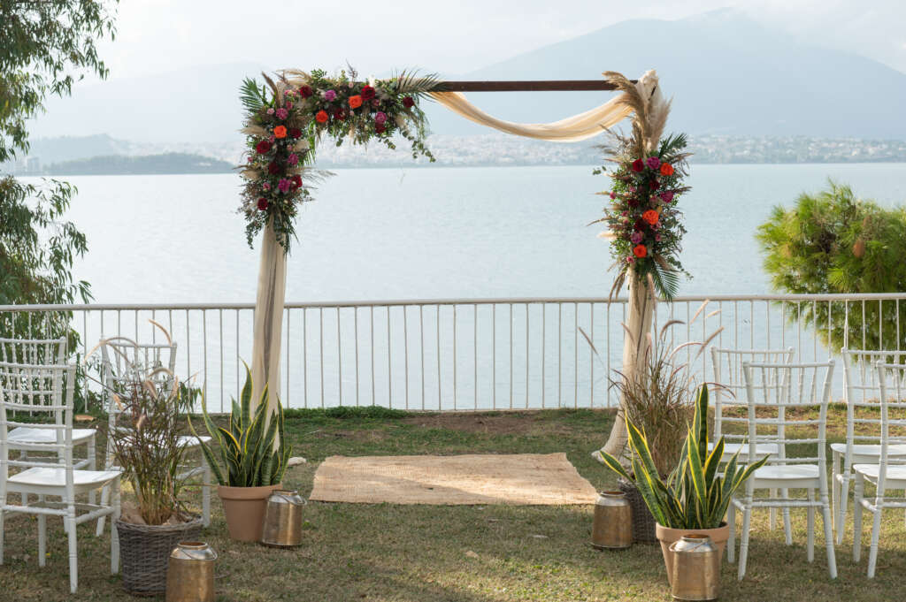 a wooden arch, overlooking the sea, draped in flowing fabric covered in rich coloured flowers