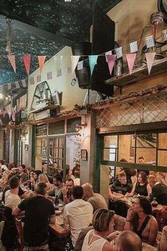 Corporate group enjoying a festive dinner at an authentic Greek tavern with colorful bunting, team bonding and culinary experience in Greece produced by Sirtaki Events.